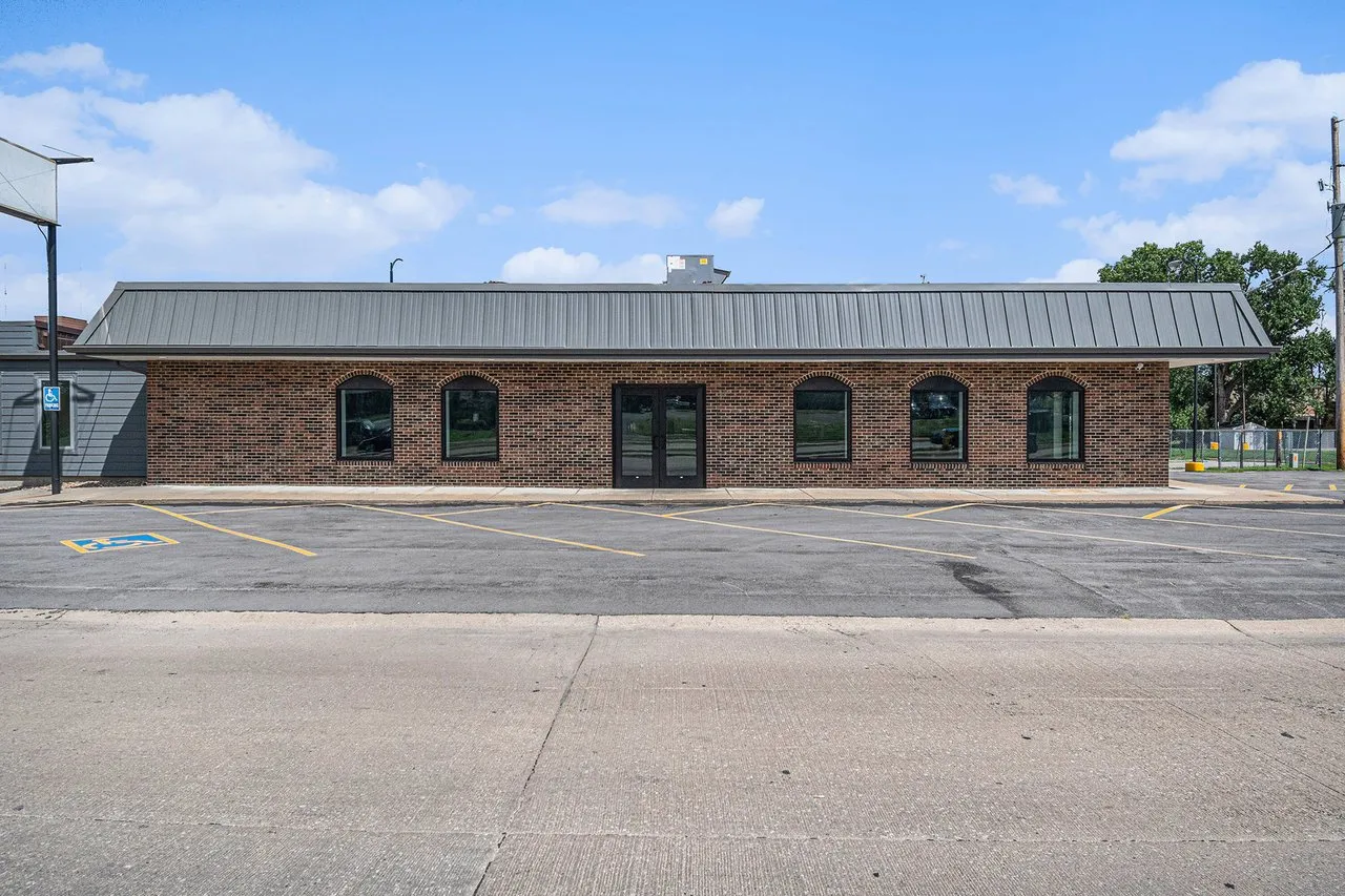 Single-story brick commercial building with a gray metal roof and parking lot.
