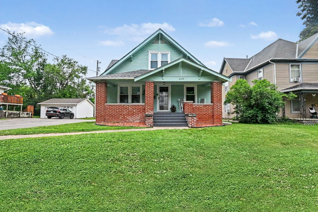 Mint-green two-story house with a brick-front porch and broad lawn.