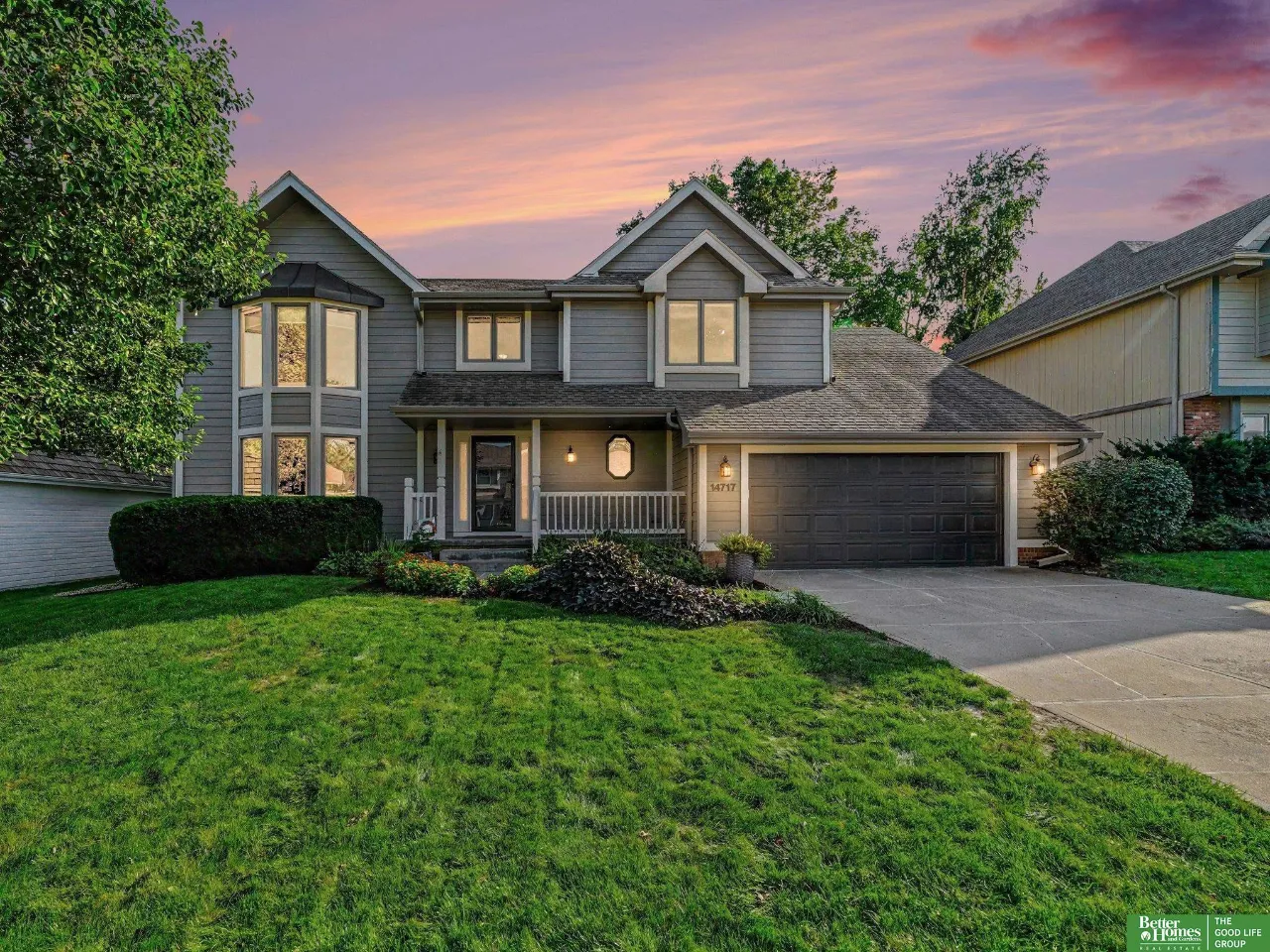 Gray two-story house with an attached garage and covered porch at dusk.